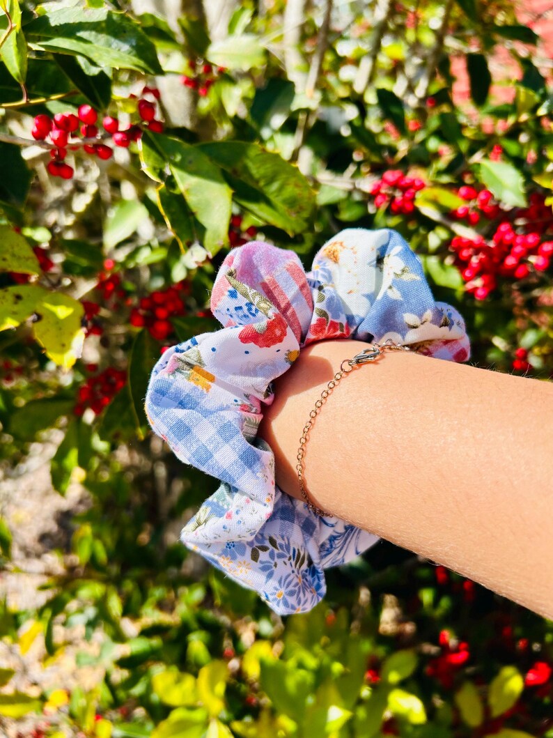 Może przedstawiać: Wielowzorzysta gumka do włos&oacute;w w odcieniach niebieskiego, białego, r&oacute;żowego i czerwonego. Gumka ma wzory kwiatowe, w kratkę i inne. Widoczna jest r&oacute;wnież bransoletka z łańcuszkiem w kolorze złotym.