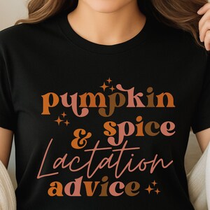 May include: Black t-shirt with the words "Pumpkin & Spice Lactation Advice" in orange, pink, and brown script. The shirt has a crew neck and short sleeves. The text is in a retro font.