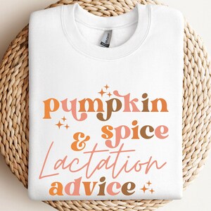 May include: White crewneck sweatshirt with the text "Pumpkin & Spice Lactation Advice" in orange, brown, and pink lettering. The sweatshirt is displayed on a round woven basket.