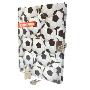 May include: A black and white soccer ball patterned diary with a silver lock and key. The diary has the word "CHAMPION" printed on the front cover.