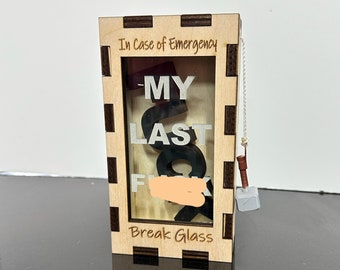 May include: A wooden box with a glass panel and a small hammer attached to a chain. The box has the text "In Case of Emergency" and "Break Glass" printed on it. The glass panel has the words "My Last" printed on it.