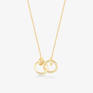 May include: A gold-colored necklace featuring two interlocking circles. One circle is smooth, while the other has a twisted rope design. The necklace hangs from a delicate chain, creating a simple yet elegant look.