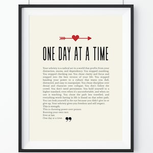 May include: Framed print with the text "ONE DAY AT A TIME" in bold black letters. A red heart and arrow design is above the text. The print includes a motivational message about sobriety and self-respect.