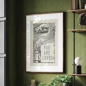 May include: A framed black and white print with an intricate design and the text "You are loved". The print is hanging on a green wall in a room with a wooden desk, a chair, and a window.