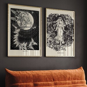 May include: Two black and white framed prints with a vintage aesthetic. The print on the left features a stylized image of a woman with wings and a crescent moon. The print on the right features a stylized image of a woman standing in a forest. Both prints have the text "Darby & Holt" at the bottom.