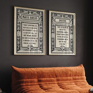 May include: Two black and white framed prints with inspirational quotes from Marcus Aurelius and Epictetus. The quotes are printed in a vintage style font and are surrounded by ornate borders. The prints are hanging on a dark gray wall.