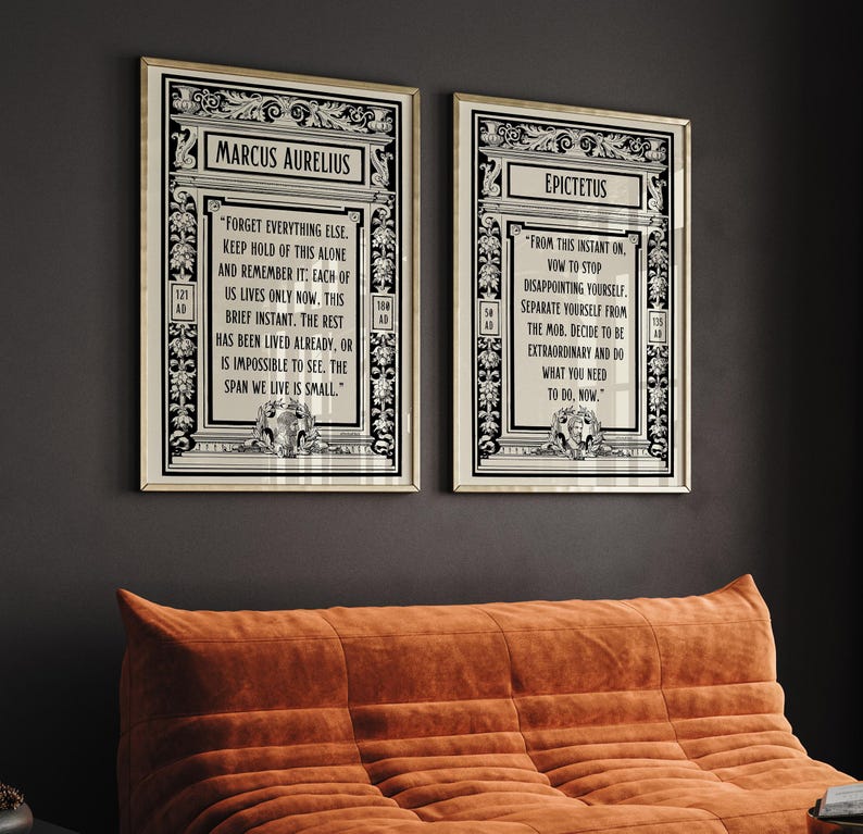 May include: Two black and white framed prints with inspirational quotes from Marcus Aurelius and Epictetus. The quotes are printed in a vintage style font and are surrounded by ornate borders. The prints are hanging on a dark gray wall.