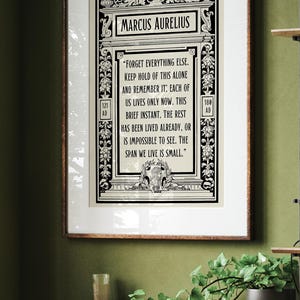 May include: Black and white framed print with a quote by Marcus Aurelius. The quote reads "Forget everything else. Keep hold of this alone and remember it: Each of us lives only now, this brief instant. The rest has been lived already, or is impossible to see. The span we live is small."