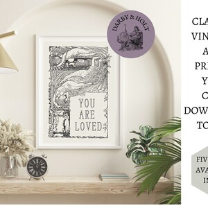 May include: A black and white vintage art print with a decorative border and the text "You Are Loved". The print is framed in a white frame and is hanging on a white wall.