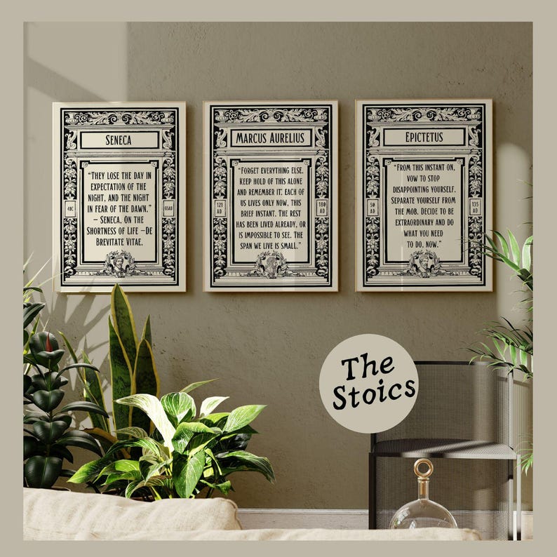 May include: Three black and white framed prints with inspirational quotes from Seneca, Marcus Aurelius, and Epictetus. The quotes are about living in the present moment and not dwelling on the past or future. The prints are arranged in a row on a wall with a light brown background. The text below the prints reads "The Stoics".
