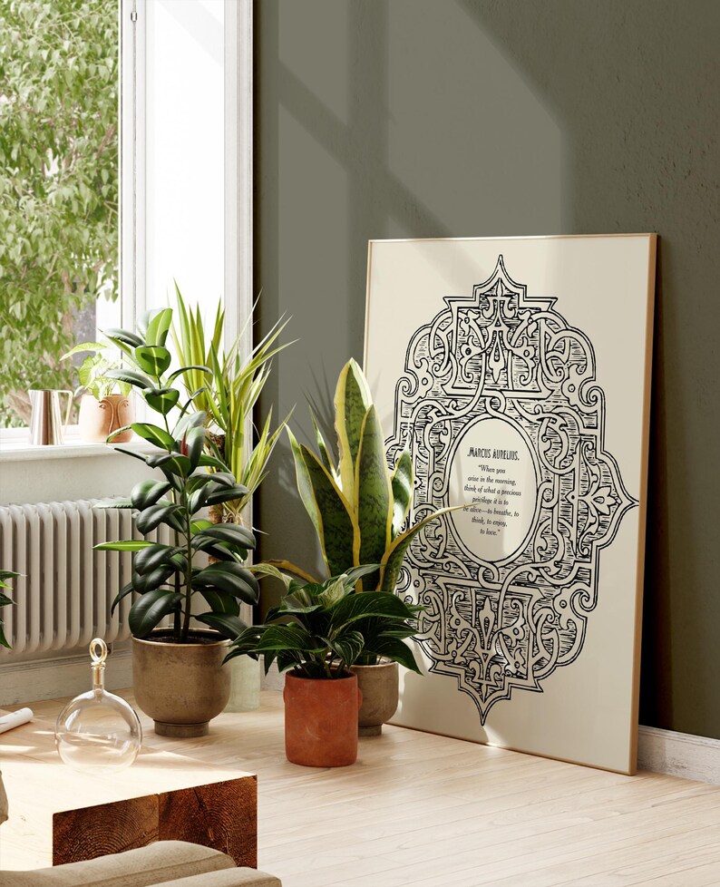 May include: A framed print with a black and white intricate design and a quote by Marcus Aurelius. The print is hanging on a green wall with two potted plants in front of it.
