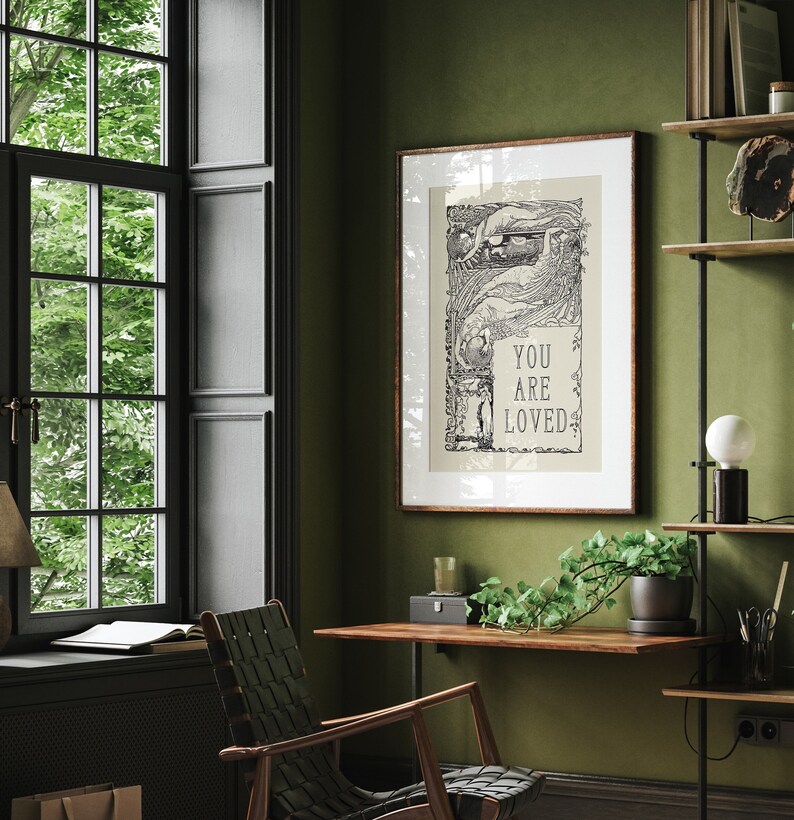 May include: A framed black and white print with an intricate design and the text "You are loved". The print is hanging on a green wall in a room with a wooden desk, a chair, and a window.