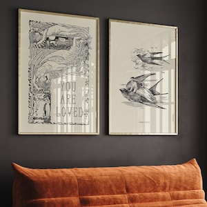 May include: Two framed black and white prints with gold frames. The print on the left features a woman with wings and the text "You are loved". The print on the right features a bird with a woman riding on its back.