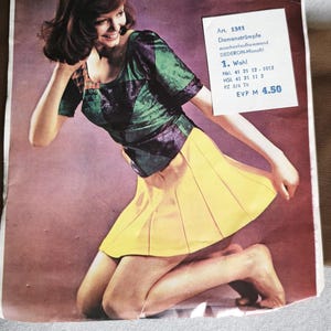 Puede incluir: Un anuncio de producto vintage de medias Ursus con una persona que viste una blusa de manga corta con estampado verde y negro y una falda plisada amarilla. El empaque incluye el texto Ursus Strümpfe, Damenfeinstrumpf y detalles del producto.