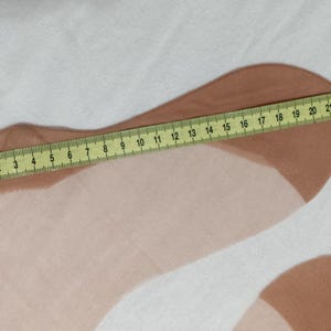Peut inclure: Une paire de bas transparents de couleur chair avec des zones renforcées au niveau des orteils et du talon. Un mètre ruban jaune est placé sur la longueur d'un bas, indiquant une mesure d'environ 24 cm du talon à la pointe.