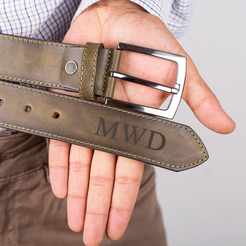 May include: A green leather belt with a silver buckle and the initials "MWD" engraved on the strap.