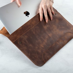 May include: A brown leather laptop sleeve with the text "Dream Big" embossed on the front. A silver laptop is partially inside the sleeve.