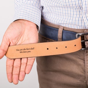 May include: A brown leather belt with a blue buckle. The belt has an engraved message that reads "You are the best dad! We love you."