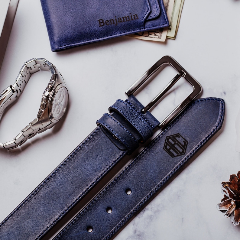 May include: A dark blue leather belt with a silver buckle and a monogrammed initial. The belt is made of high-quality leather and has a classic design.