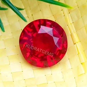 Peut inclure: Une pierre précieuse ronde rouge vif avec une taille facetée. La pierre précieuse est sur un fond jaune tissé.