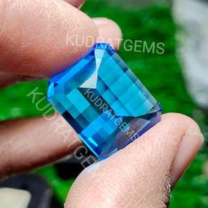 Puede incluir: Una gema azul vibrante con forma rectangular y corte facetado. La gema se sostiene en una mano, mostrando su brillo y claridad.