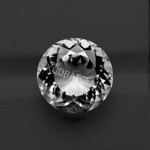 May include: A round, faceted, clear gemstone with a brilliant cut, displaying multiple triangular and kite-shaped facets that reflect light. The word KUDRATGEMS is printed in white across the center of the stone, which is set against a dark background.