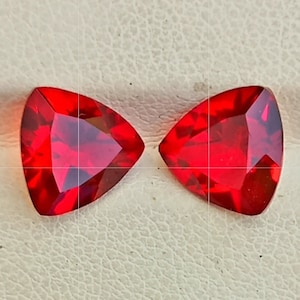 May include: Two red triangular gemstones with a faceted cut.
