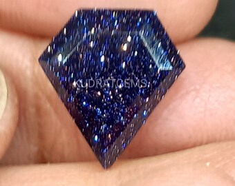 May include: A diamond-shaped blue sandstone gemstone featuring a deep navy blue base with numerous sparkling metallic flecks throughout. The surface of the stone is faceted and displays the text KUDRATGEMS printed in white across the center.