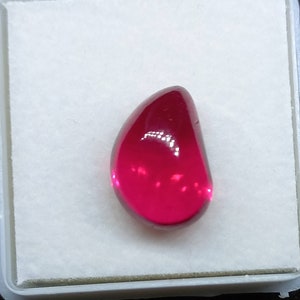 May include: A teardrop-shaped, deep red gemstone with a smooth, polished surface.