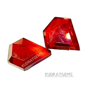 May include: Two red gemstones with a faceted cut. The gemstones are on a white background. The text "KUDRATGEMS" is visible on the image.