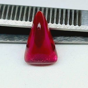 May include: A triangular, deep red gemstone with a shiny, polished surface.