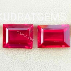 Könnte beinhalten: Zwei leuchtend rote rechteckige Edelsteine, wahrscheinlich Rubine, werden in einer weißen Schachtel mit dem aufgedruckten Text "KUDRATGEMS" auf der Oberseite präsentiert.