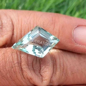 Può includere: Una pietra preziosa di acquamarina blu chiaro con forma di aquilone e taglio sfaccettato. La pietra preziosa è tenuta in una mano.