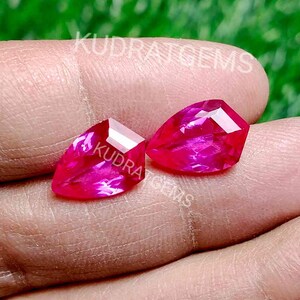 Könnte beinhalten: Zwei rosafarbene birnenförmige Edelsteine mit facettiertem Schliff werden in einer Hand gehalten. Die Edelsteine sind etwa 2,5 cm lang.