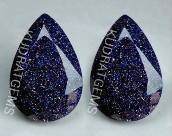 May include: Two pear-shaped blue sandstone gemstones with a dark, glittery surface and faceted edges. The text KUDRATGEMS is printed vertically across each stone in white lettering, highlighting the deep blue color and reflective sparkles.