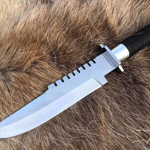May include: A silver and black hunting knife with a serrated blade and a black paracord handle.