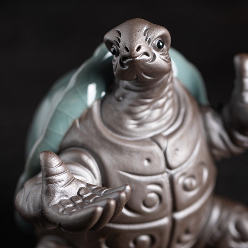 May include: A ceramic turtle figurine with a detailed, textured shell and outstretched arms. The turtle is painted in a dark brown glaze with a hint of green on the shell.