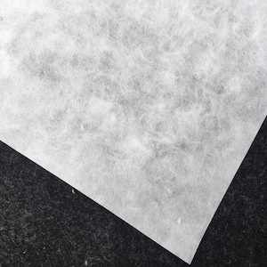 May include: A white, textured, paper sheet with a slightly rough surface. The paper is folded in half and the corner is visible.