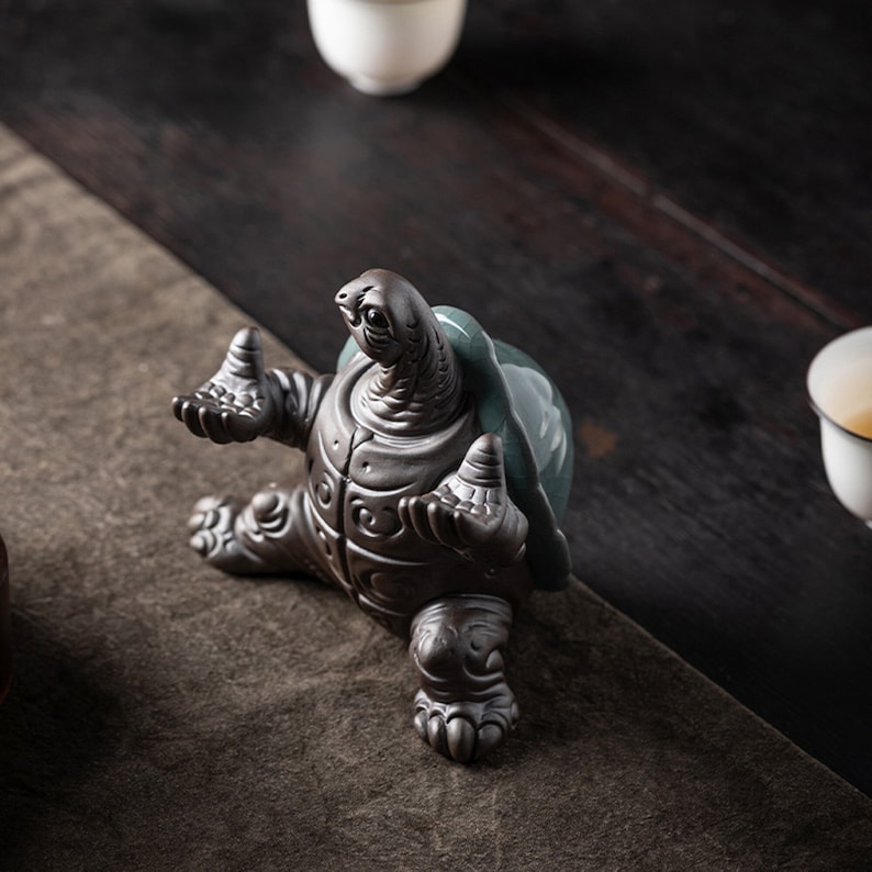 May include: A ceramic turtle figurine with a green shell and brown body. The turtle is sitting on its hind legs with its front legs outstretched. The figurine is a decorative piece for a home or office.