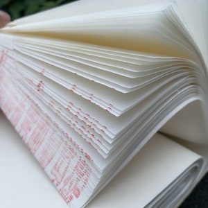May include: A close-up of a white notebook with red markings on the pages. The notebook is open and the pages are fanned out.