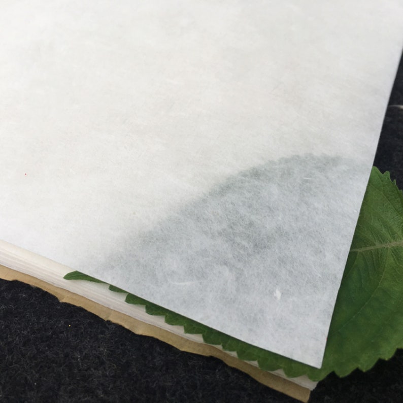 May include: A stack of white, textured paper sheets with a green leaf partially visible at the bottom.