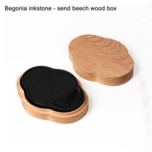May include: A black inkstone in a wooden box. The box is made of beech wood and has a cloud-shaped design. The inkstone is also cloud-shaped and has a rough, textured surface.