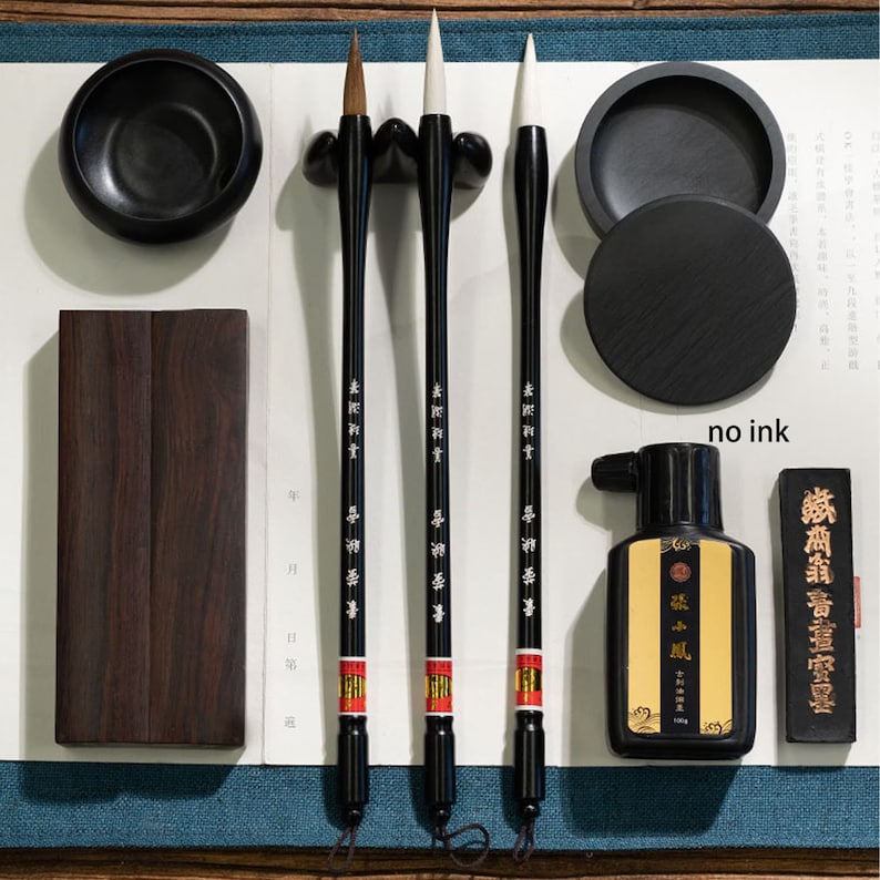 May include: Three black calligraphy brushes with white bristles, a black ink bottle, a black ink stick, and two black ink stones. The brushes have Chinese characters written on them. The ink bottle has a label that says "墨汁" in Chinese characters. The ink stick has Chinese characters written on it. The ink stones are round and have a smooth surface.