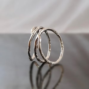 Puede incluir: Tres anillos de plata con un acabado texturizado, apilados uno encima del otro.