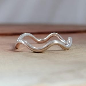 Könnte beinhalten: Ein silberner Wellenring mit einem wellenförmigen Design. Der Ring ist aus Metall und hat eine glatte Oberfläche.