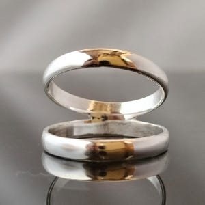 May include: Two silver wedding bands stacked on top of each other. The bands are smooth and shiny.