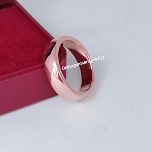 Puede incluir: Una banda de boda de oro rosa con un acabado liso y pulido. La banda es gruesa y tiene un perfil redondeado.