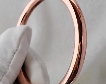 May include: A simple, polished copper bangle bracelet. The bracelet is round and has a smooth, shiny finish.