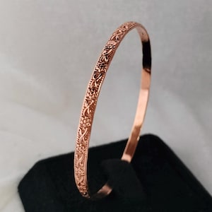 May include: A rose gold bangle bracelet with a delicate floral design. The bracelet is thin and has a polished finish.