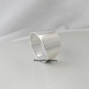Könnte beinhalten: Ein breiter, silberfarbener Ring mit glatter, polierter Oberfläche. Der Ring hat eine zylindrische Form und ein minimalistisches Design. Der Text "Dishgemsandjewelry" ist sichtbar.